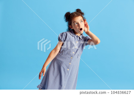 Portrait of lovely little girl, child with curly hair and cute hairdo posing against blue studio background. Overhearing 104836627