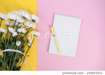 A clean notebook and pen on a light pink table. Mockup with a bouquet of flowers on a yellow table A clean notebook and pen on a light pink table. Mockup with a bouquet of flowers on a yellow table 104841015