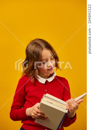 Portrait of happy schoolgirl reading a book on yellow studio 104841522