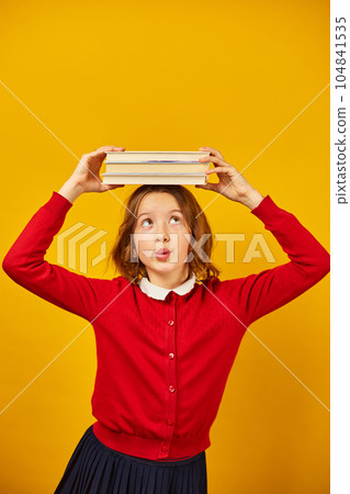 Portrait of happy teenage schoolgirl in uniform holding books on head 104841535