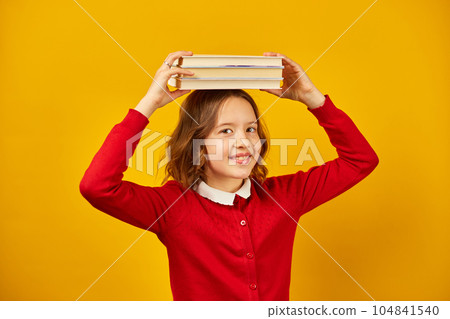 Portrait of happy teenage schoolgirl in uniform holding books on head 104841540