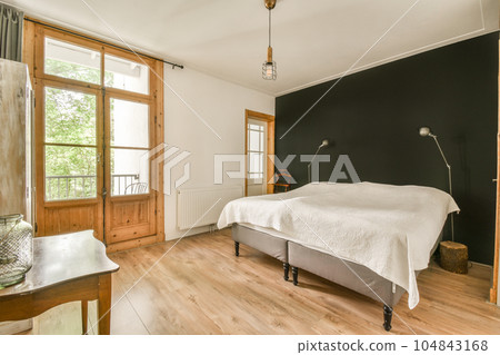 a bedroom with wood flooring and white sheets on the bed, windows in the room are open to the outside 104843168