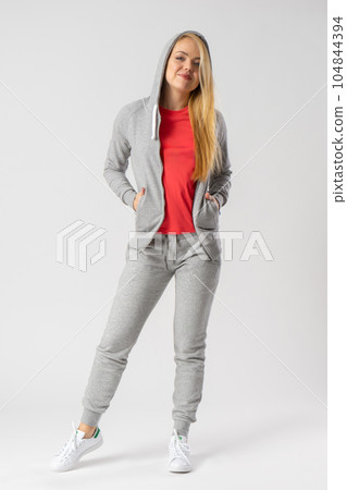 A young blonde in a gray tracksuit, red tank top and white sneakers. 104844394