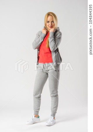 A young blonde in a gray tracksuit, red tank top and white sneakers. 104844395