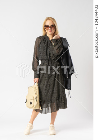 A woman in sunglasses and a casual dress holds a jacket and backpack in her hands A woman in sunglasses and a casual dress holds a jacket and backpack in her hands 104844432