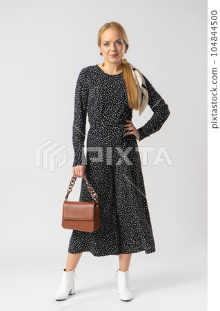 A woman in an elegant black suit with white polka dots, with a women's handbag. A woman in an elegant black suit with white polka dots, with a women's handbag. 104844500