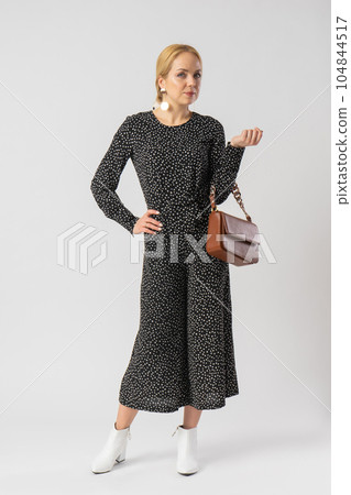A woman in an elegant black suit with white polka dots, with a women's handbag. 104844517