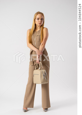Young blonde woman in an elegant casual trouser suit with a women's handbag. Young blonde woman in an elegant casual trouser suit with a women's handbag. 104844524