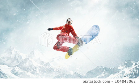 In motion. Flying high. Sportive man riding snowboard over snowy mountains background. Warm sunny day In motion. Flying high. Sportive man riding snowboard over snowy mountains background. Warm sunny day 104845062