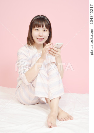 A woman in pajamas who operates a smartphone A woman in pajamas who operates a smartphone 104845217