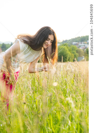 A young woman walks across a field. A walk in nature in the summer. A young woman walks across a field. A walk in nature in the summer. 104845699