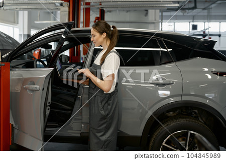 Woman auto mechanic checking customer car using laptop for diagnostics 104845989