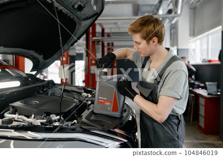 Motor oil replacement concept, young male mechanic changing engine liquid 104846019