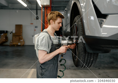 Professional man mechanic changing car wheel using electric drill Professional man mechanic changing car wheel using electric drill 104846030