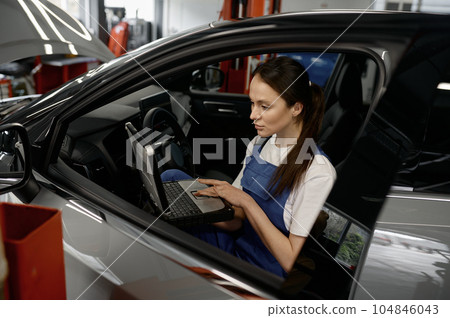 Woman technician sitting in car working on laptop providing computer diagnostics 104846043