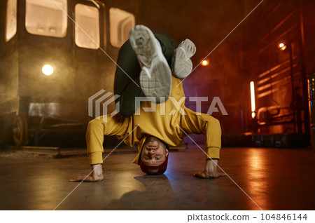 Young man freestyle dancer standing on head doing acrobatic stunt 104846144