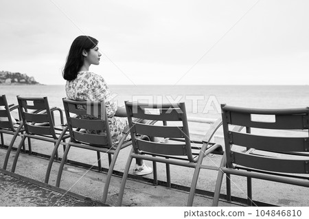 Beautiful smiling young mixed race woman sitting at one of the famous blue chairs at the Promenade des Anglais in Nice, France 104846810