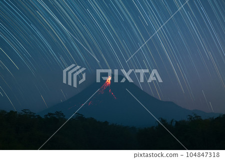 Mount Merapi volcano eruption glowing lava flow at night with star trail background, Java, Indonesia 104847318