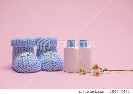 Still life with blue baby booties and small white mockup bottles of plant-based newborn cosmetics, isolated on pink 104847421