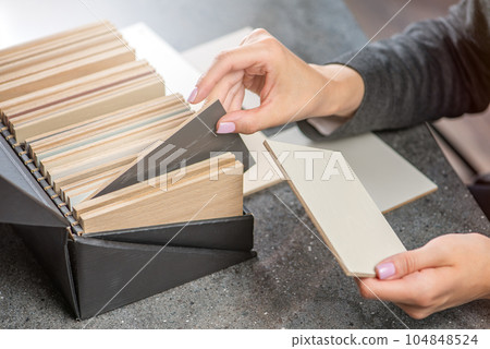 A woman interior designer chooses a color sample from chipboard. The choice of wood material for the interior project from chipboard or natural wood samples. Design or architecture concept. 104848524