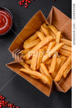 Delicious crispy french fries with salt and spices in a cardboard box Delicious crispy french fries with salt and spices in a cardboard box 104849386