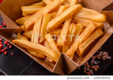 Delicious crispy french fries with salt and spices in a cardboard box 104849403