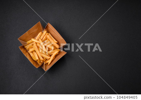 Delicious crispy french fries with salt and spices in a cardboard box 104849405