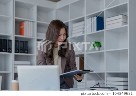 Portrait of a thoughtful Asian businesswoman looking at financial statements and making marketing plans using a computer on her desk. Portrait of a thoughtful Asian businesswoman looking at financial statements and making marketing plans using a computer on her desk. 104849681