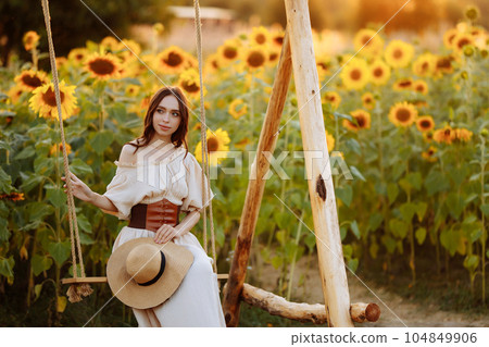 Woman in a dress in a field of sunflowers on a swing Woman in a dress in a field of sunflowers on a swing 104849906