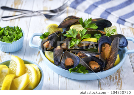 Steamed Mussels in shells in a blue plate with herbs and lemon. White wooden background. 104850750