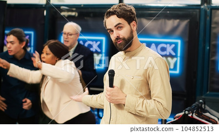 News reporter in crowded clothing store holding microphone and broadcasting black friday crazy behaviour. TV journalist creating live newscast on scene at local shopping center. 104852513