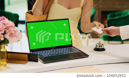 Laptop with greenscreen display on hotel front desk next to lounge area, modern isolated chromakey template at reception. Blank mockup copyspace screen on pc in tropical resort lobby. 104852652