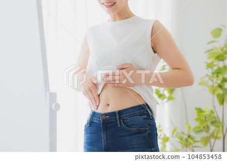 Woman checking her stomach in the mirror Woman checking her stomach in the mirror 104853458