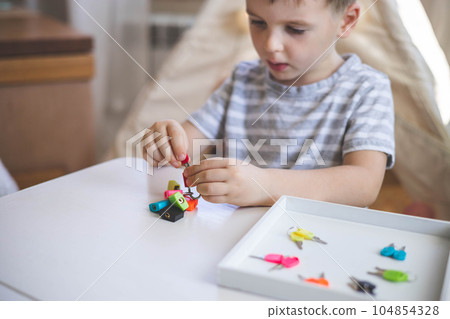 The child works with Montessori material with colored locks. Picks up keys. Develops fine motor skills. 104854328