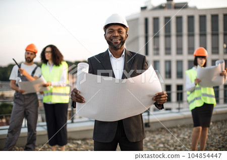 Investor posing at camera while colleagues inspecting object Investor posing at camera while colleagues inspecting object 104854447