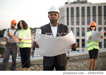 Investor posing at camera while colleagues inspecting object 104854450