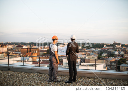 Male builders talking about real estate project on terrace 104854485