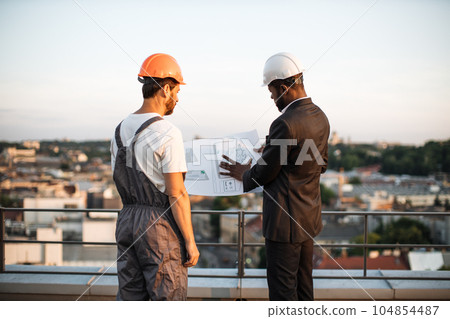 Workman presenting blueprints to urban planner on rooftop 104854487