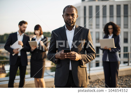 Business partners standing with remote gadgets on fresh air Business partners standing with remote gadgets on fresh air 104854552