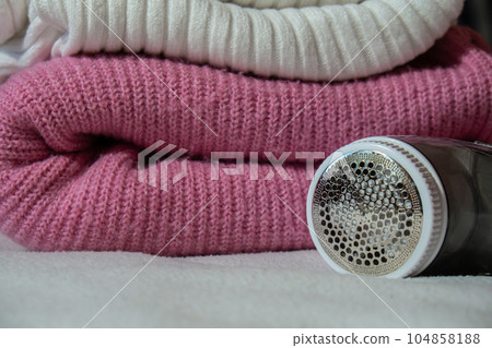 Anti-pilling razor. Device for shaving clothes. Anti-Plush fabric Shaver. Electric portable sweater pill defuzzer Lint remover from pink acrylic or wool sweater. Electric device fabric shaver after Anti-pilling razor. Device for shaving clothes. Anti-Plush fabric Shaver. Electric portable sweater pill defuzzer Lint remover from pink acrylic or wool sweater. Electric device fabric shaver after 104858188