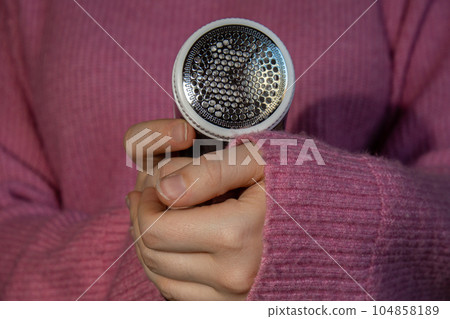 Woman using Anti-pilling razor at home. Device for shaving clothes. Anti-Plush fabric Shaver. Electric portable sweater pill defuzzer Lint remover from pink acrylic or wool sweater. Slow fashion Woman using Anti-pilling razor at home. Device for shaving clothes. Anti-Plush fabric Shaver. Electric portable sweater pill defuzzer Lint remover from pink acrylic or wool sweater. Slow fashion 104858189