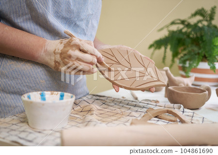 woman forming leaf shaped clay by hands, closeup in artistic studio 104861690