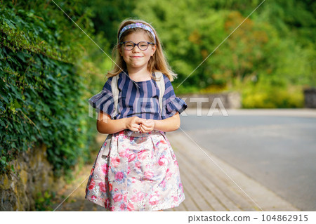 Little Preschool Girl on the Way to School. Healthy Happy Child Walking to Nursery School and Kindergarten. Smiling Child with Eyeglasses and Backpack on the City Street, Outdoors. Back to School. 104862915