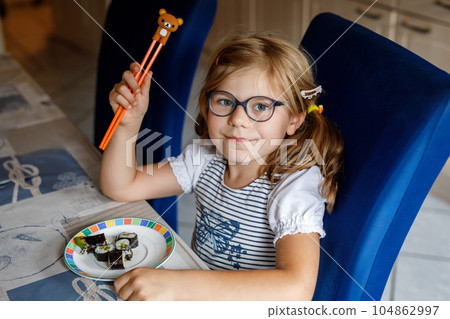Happy Preschool Girl Eating Sushi Rolls at Home Using Chopsticks. Healthy Food for Children and Youth. Cute Child Tasting Japanese Food. Little Child with Eyeglasses Enjoying Meal. Happy Preschool Girl Eating Sushi Rolls at Home Using Chopsticks. Healthy Food for Children and Youth. Cute Child Tasting Japanese Food. Little Child with Eyeglasses Enjoying Meal. 104862997