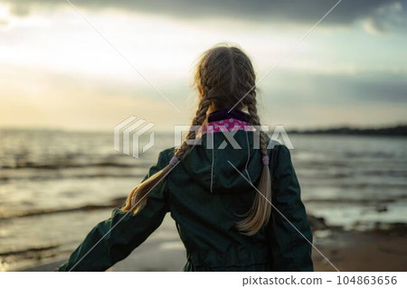 back view of caucasian blond girl with hairs styled with two plaits looking at sea on sunset back view of caucasian blond girl with hairs styled with two plaits looking at sea on sunset 104863656