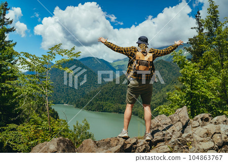 Hiking traveller man with backpack hands up enjoying beautiful view of Lake Ritsa in Abkhazia 104863767