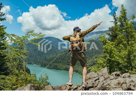Hiking traveller man with backpack hands up enjoying beautiful view of Lake Ritsa in Abkhazia 104863794