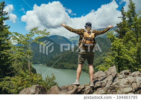 Hiking traveller man with backpack hands up enjoying beautioful view of Lake Ritsa in Abkhazia Hiking traveller man with backpack hands up enjoying beautioful view of Lake Ritsa in Abkhazia 104863795