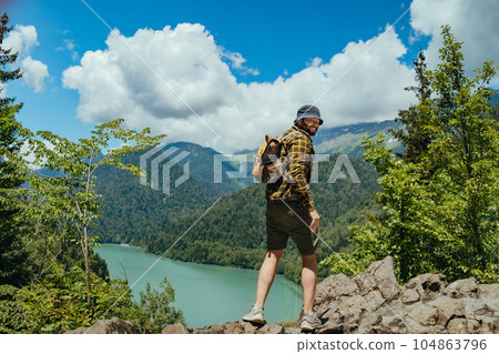 Hiking traveller handsome caucasian bearded man with backpack enjoying beautioful view of Lake Ritsa in Abkhazia Hiking traveller handsome caucasian bearded man with backpack enjoying beautioful view of Lake Ritsa in Abkhazia 104863796
