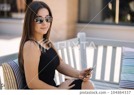 Portrait of beautiful woman using phone outdoor. Gorgeous female in beautiful black dress smile. Sunglasses  104864337